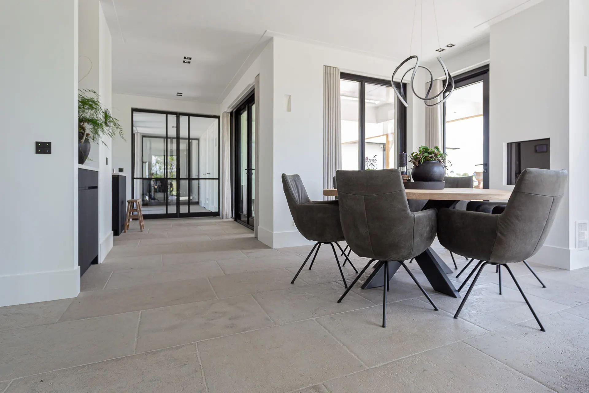Lichte woonkamer met een natuursteen vloer en een eettafel bij het raam